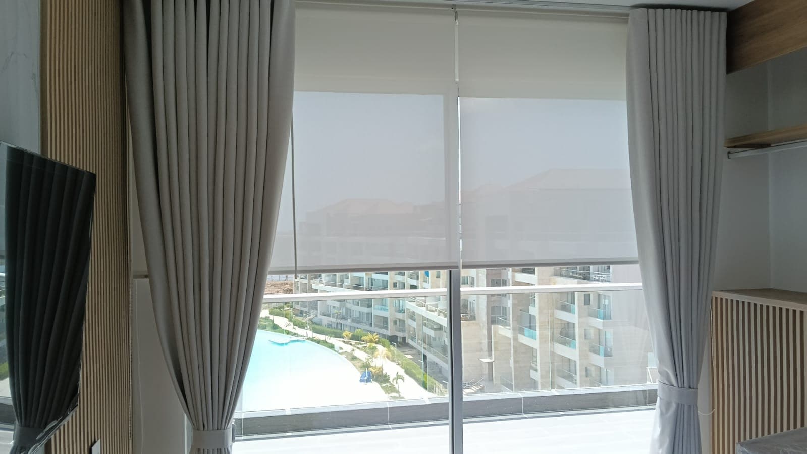 Sistema doble con cortinón gris y persiana solar screen desenrollada en sala con vista a piscina