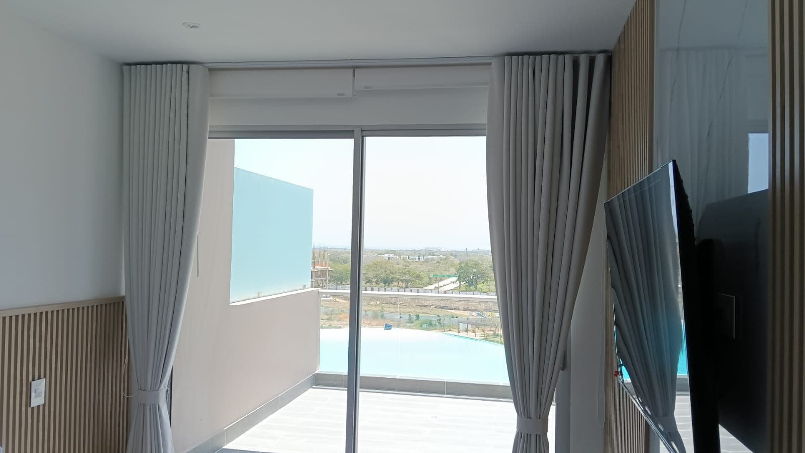 Sistema doble con cortinón blanco y persiana enrollable solar screen desenrollada en apartamento con vista a piscina, instalado por Reddy en Cartagena