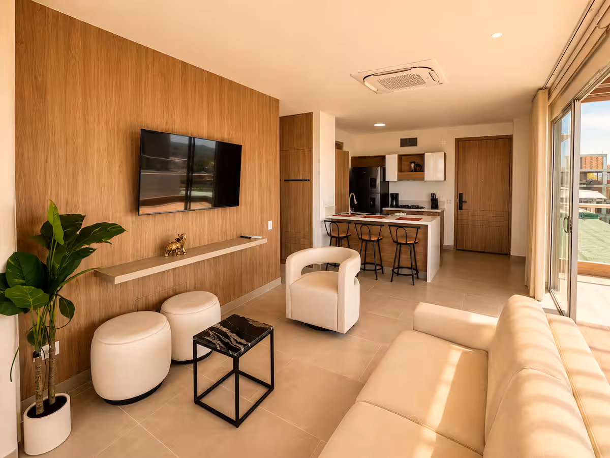Sala con pared de madera, TV, planta y cocina al fondo