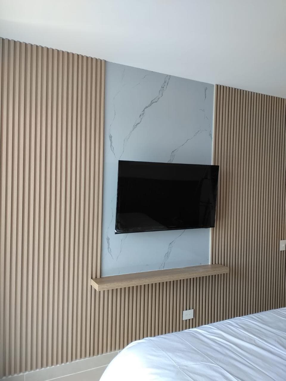 Habitación con panel de listones a los lados y recuadro de mármol con TV en el centro