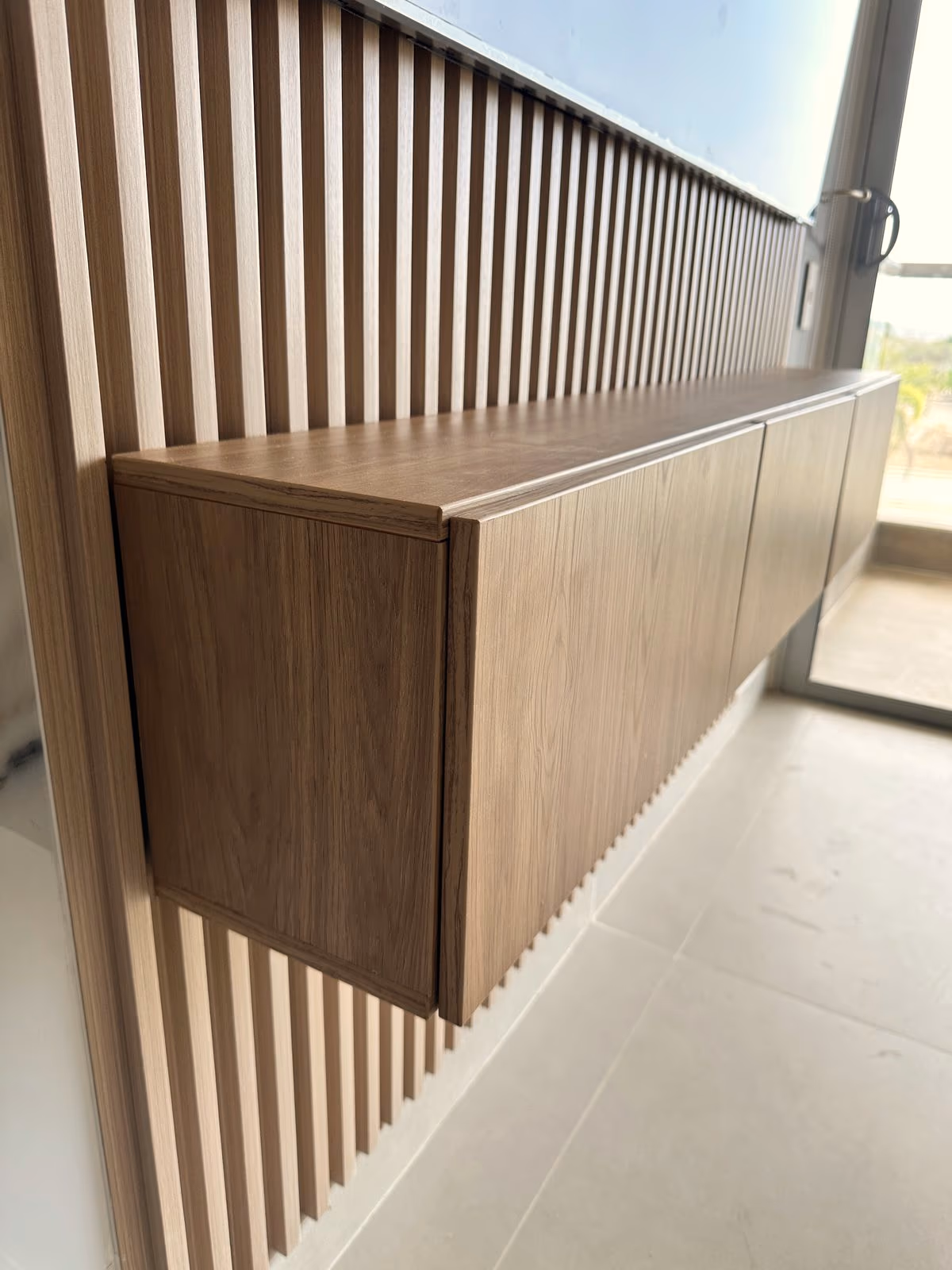 Mueble flotante de madera montado sobre un muro de listones verticales