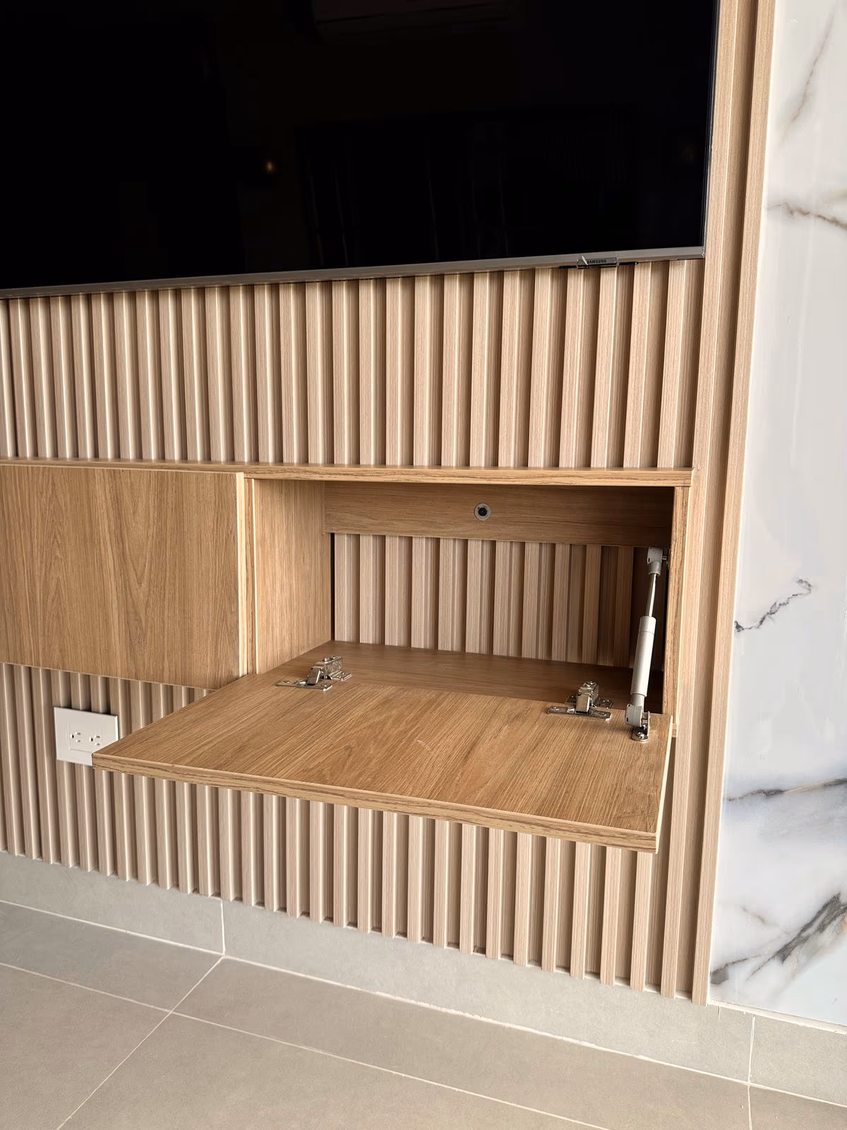 Nicho abierto en un muro de listones de madera junto a un panel de mármol