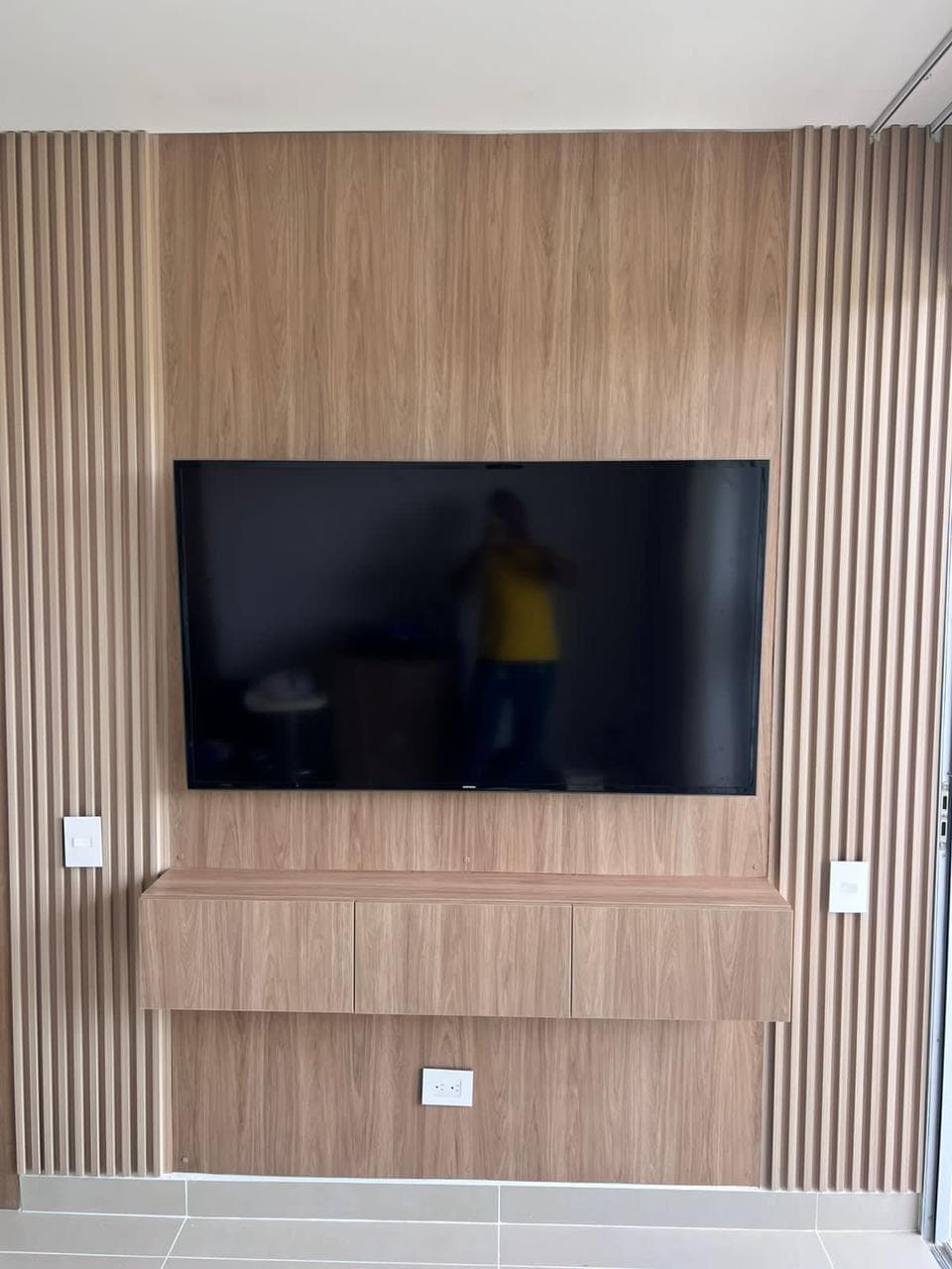 Muro de TV full-wall en listones de madera con mueble bajo y TV grande, instalado por Reddy en Cartagena