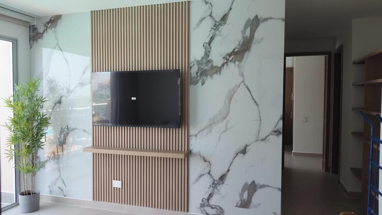 Muro de TV con panel de listones de madera enmarcado entre dos paños de mármol calacatta blanco, instalado por Reddy en Cartagena