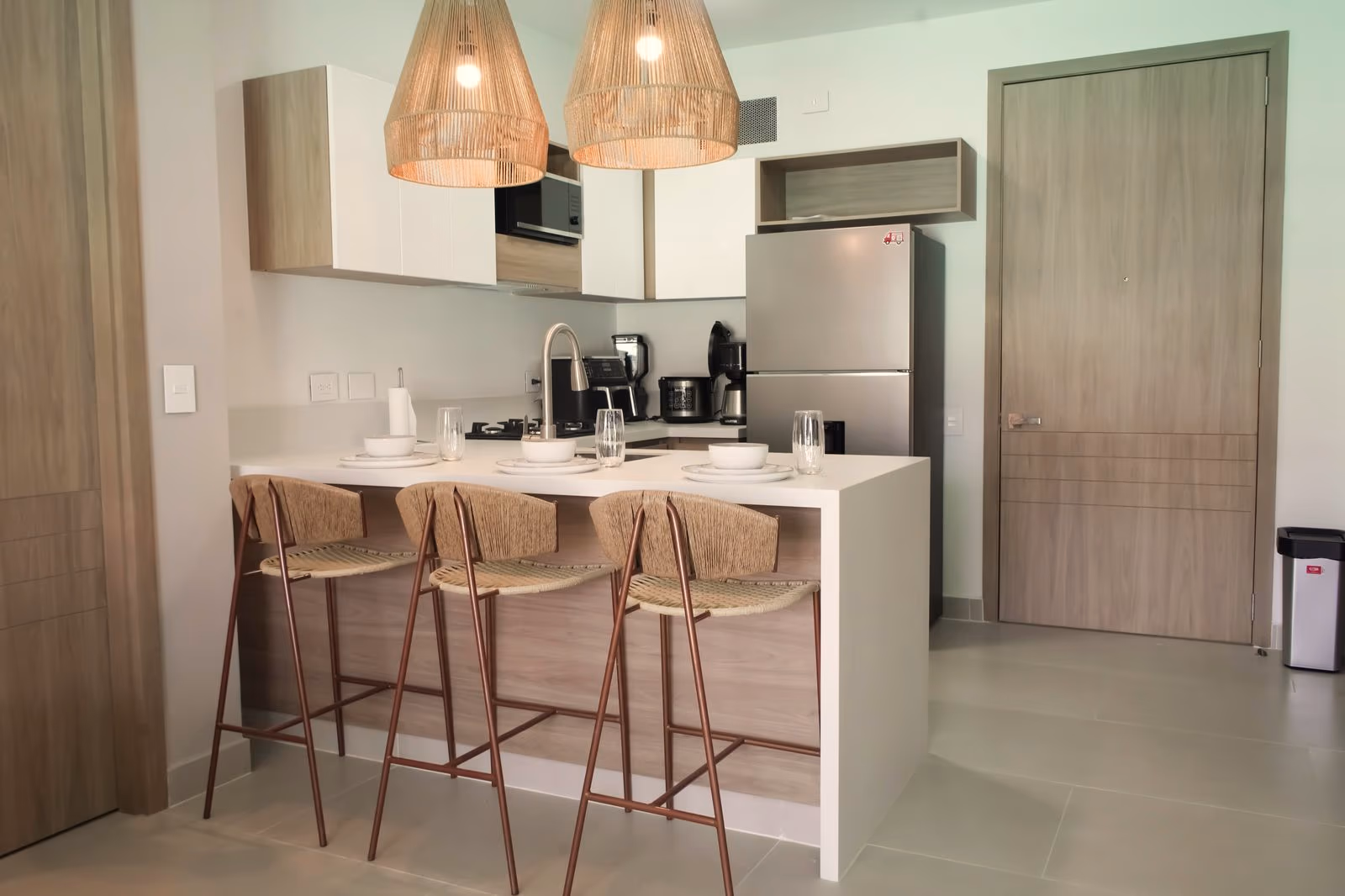 Cocina con barra, taburetes, lámparas colgantes y puerta principal