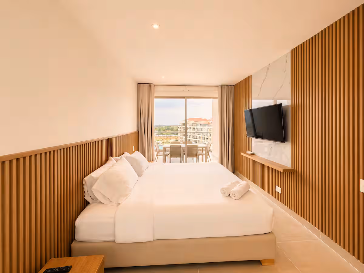 Dormitorio con panel de listones de madera completo, TV sobre mármol y balcón