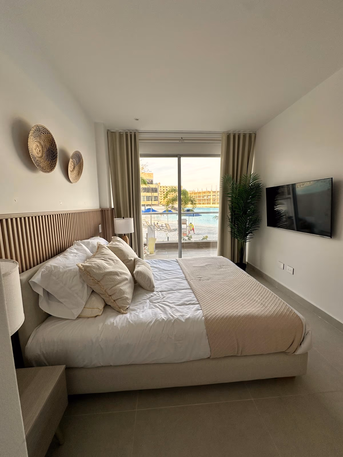 Habitación con cabecero de listones, TV, palma y vista a la laguna
