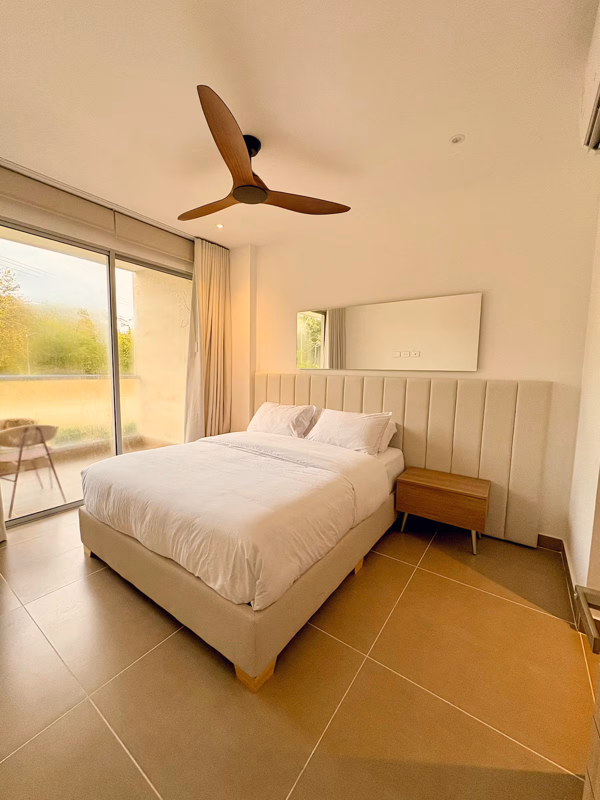 Habitación con ventilador de madera, cabecero acolchado y terraza verde
