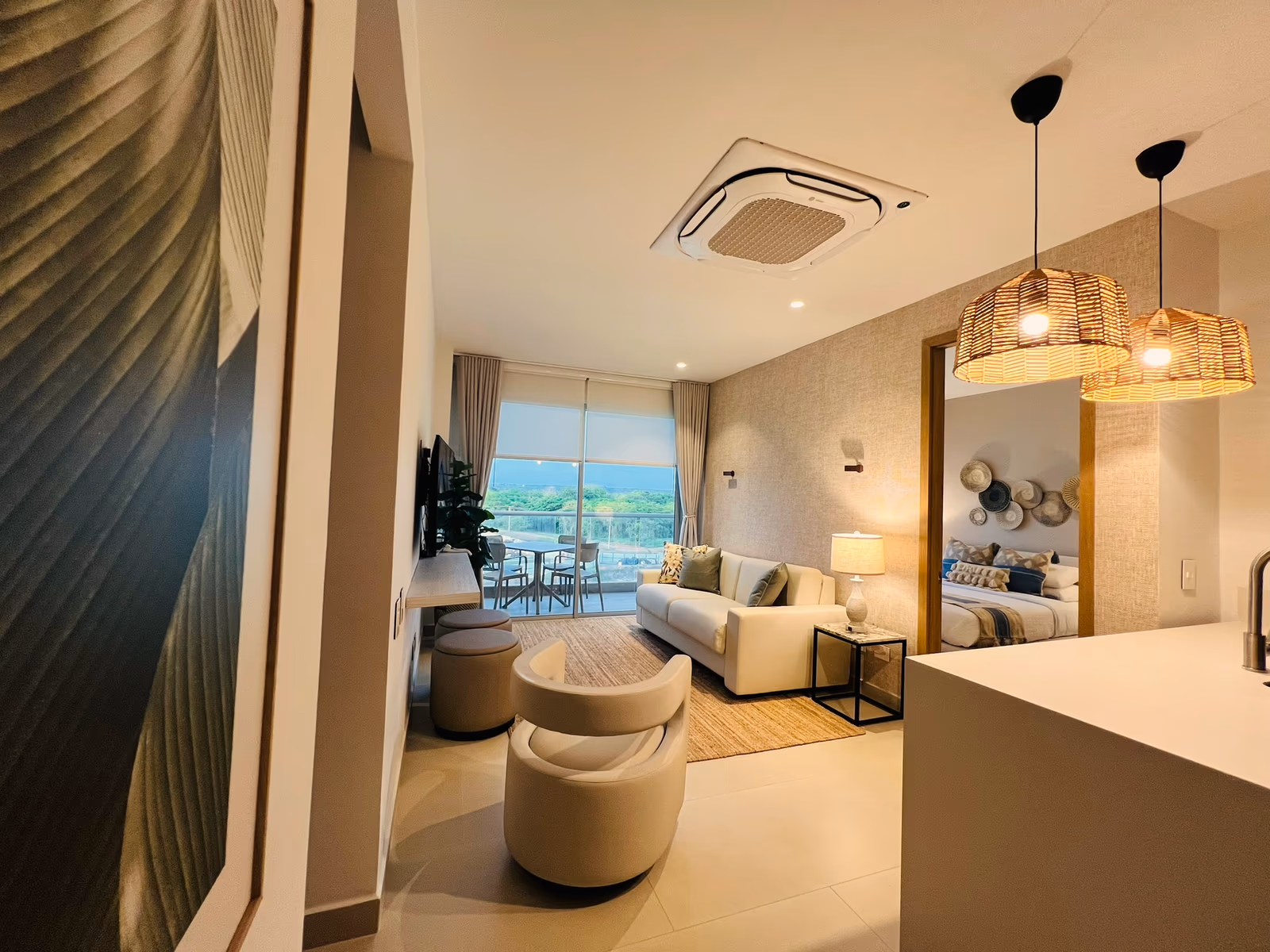 Sala vista desde la cocina con lámparas de mimbre y cuadro de hoja