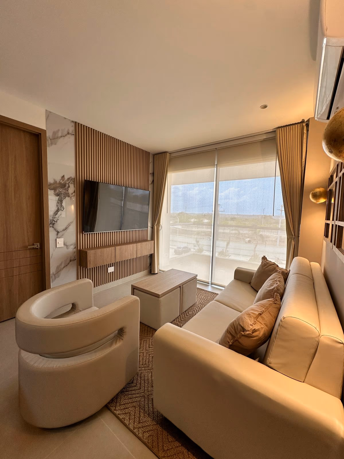 Sala con muro de mármol y listones, TV, sofá y cortinas