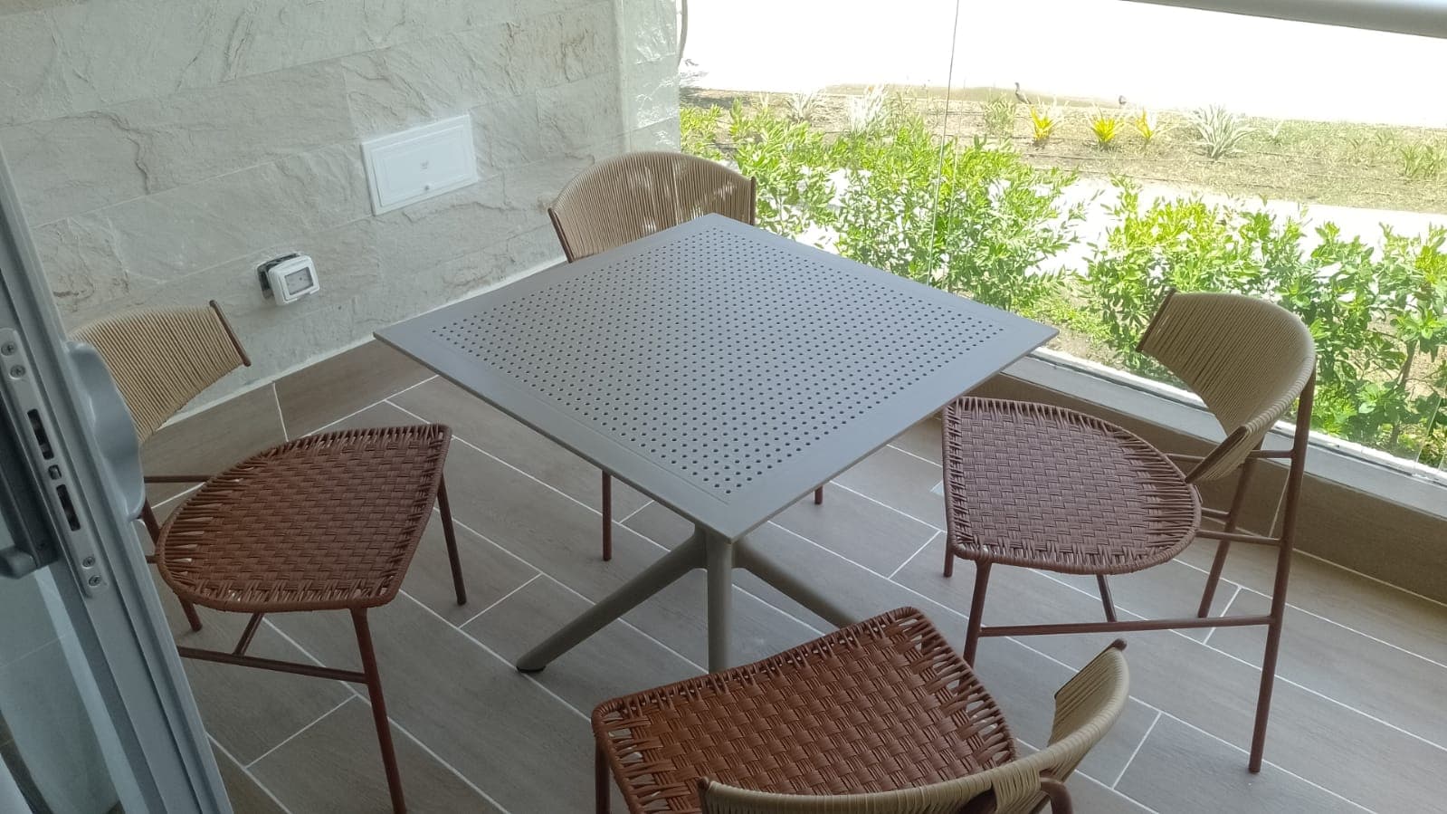 Mesa cuadrada de aluminio con sillas tejidas en cuerda terracota en terraza con vegetación