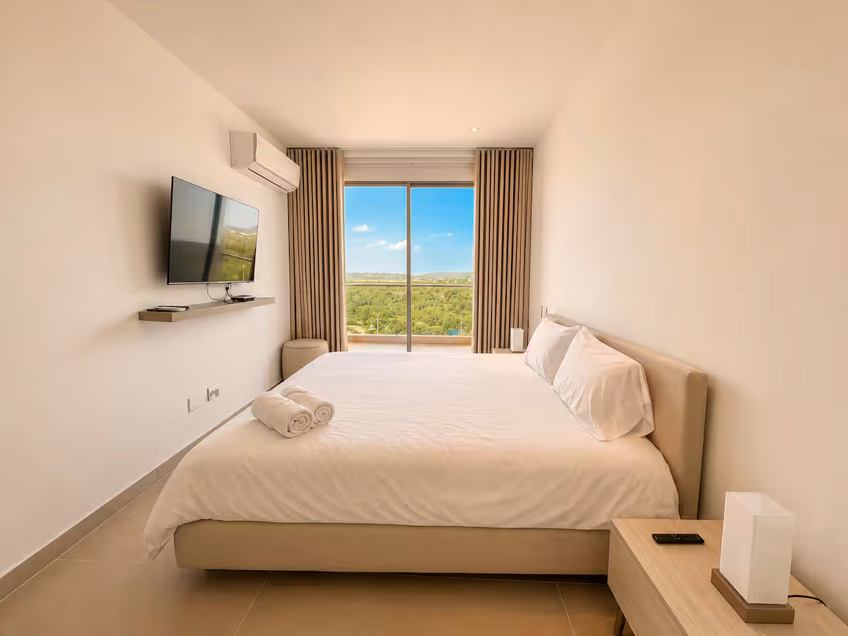 Dormitorio principal con cama king, cortinas y vista verde
