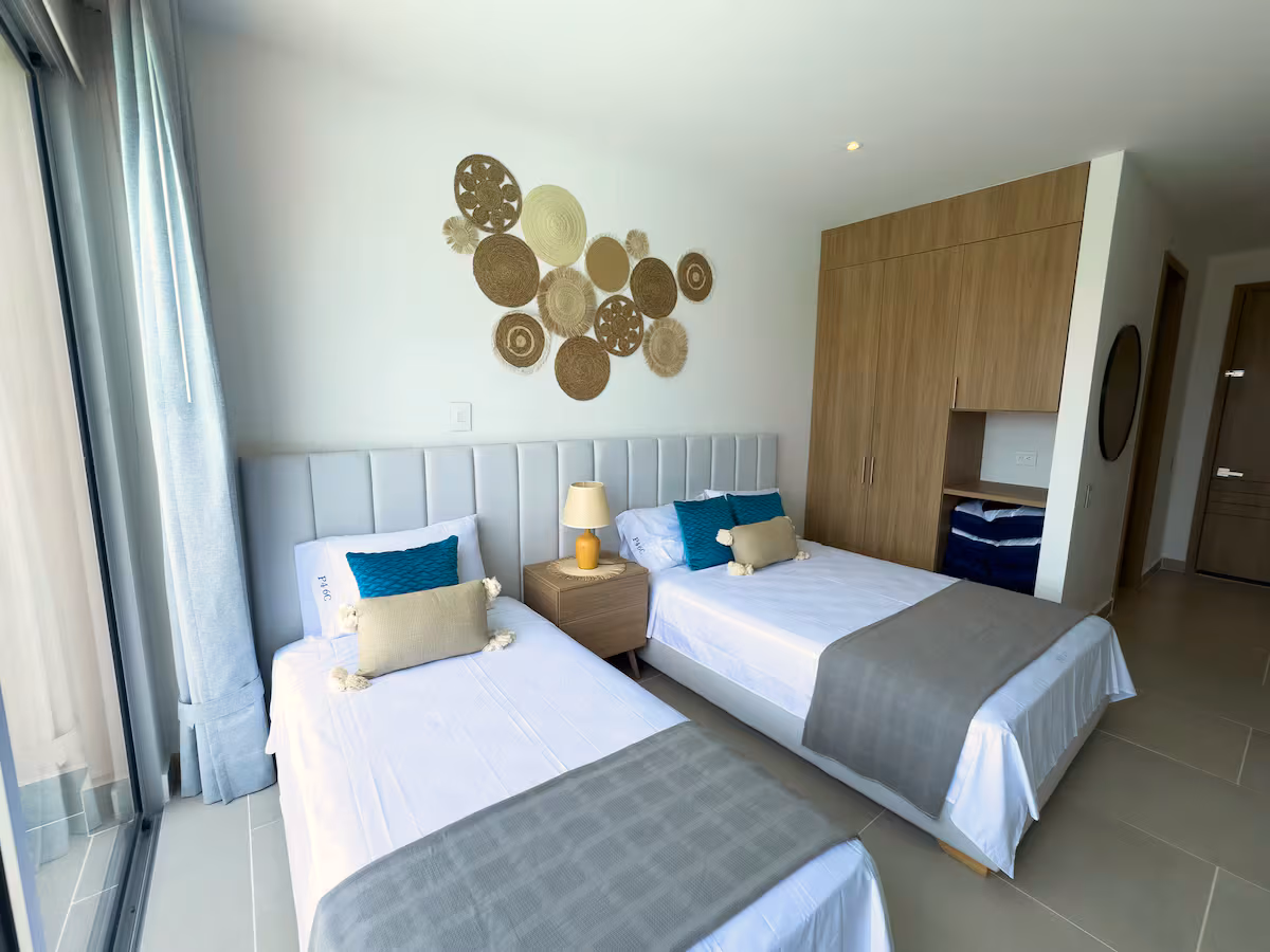 Habitación con dos camas, cojines turquesa, cestas y clóset de madera