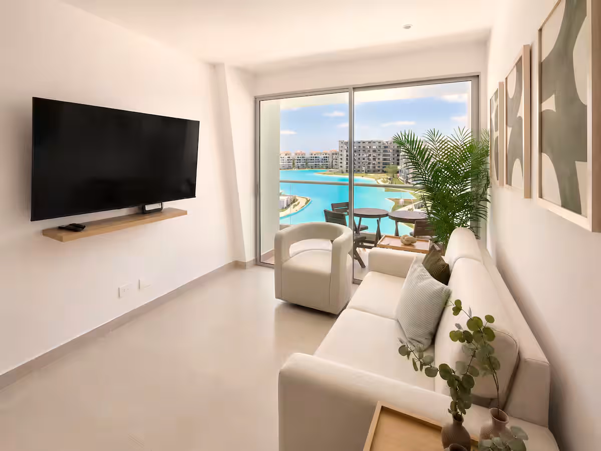 Sala minimalista con TV, sofá blanco y ventanal con vista a la laguna
